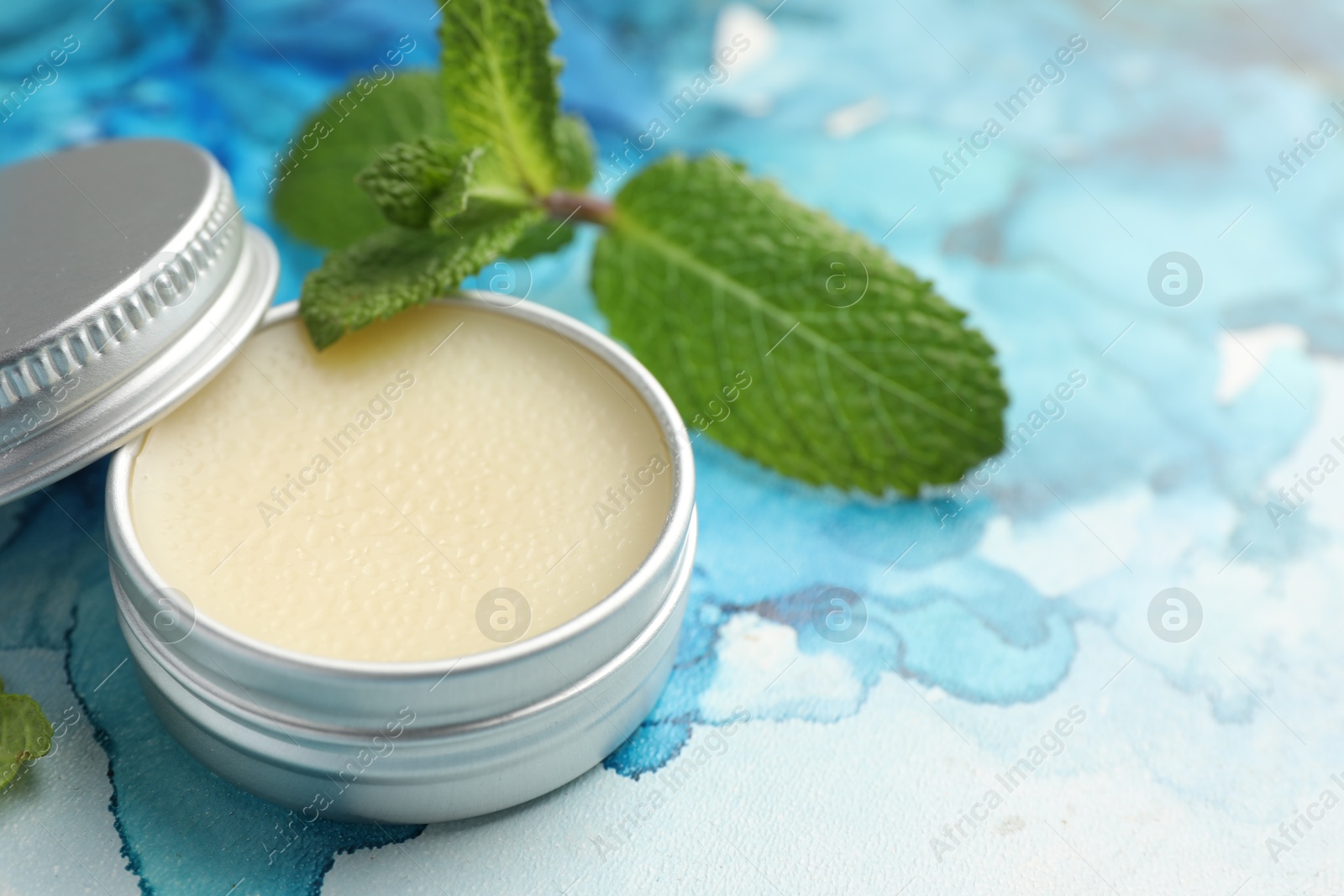 Photo of Natural lip balm and mint leaves on color background, closeup. Space for text