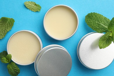 Photo of Natural lip balms and mint leaves on light blue background, flat lay