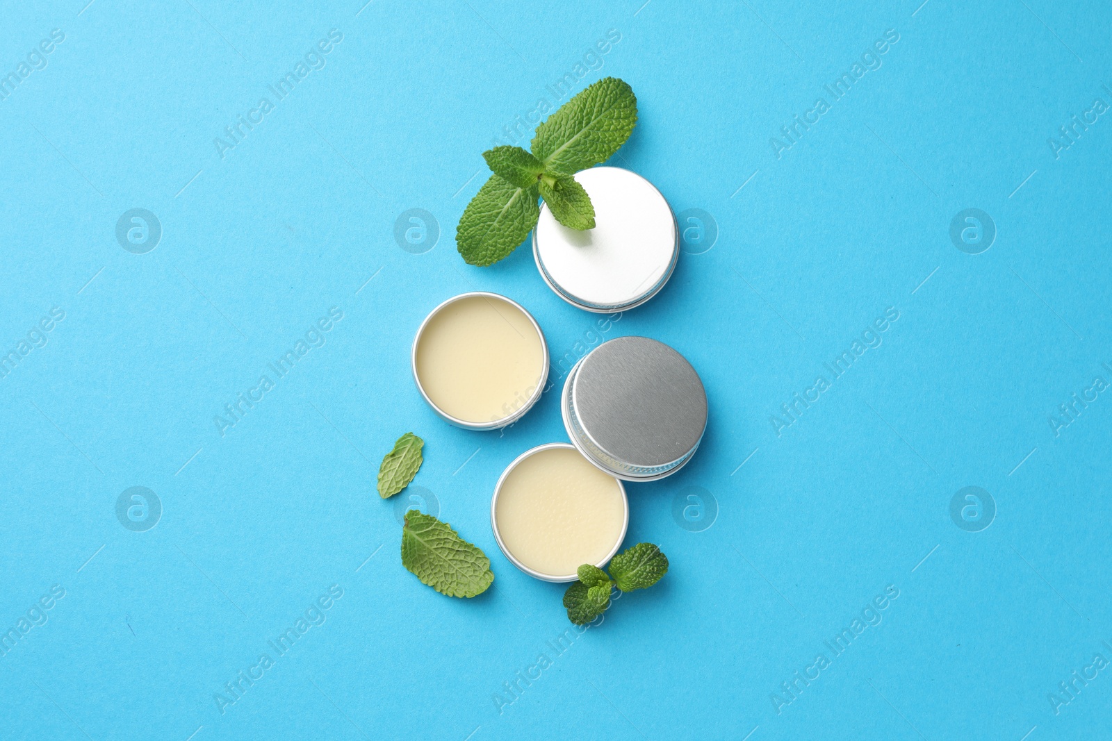 Photo of Natural lip balms and mint leaves on light blue background, flat lay