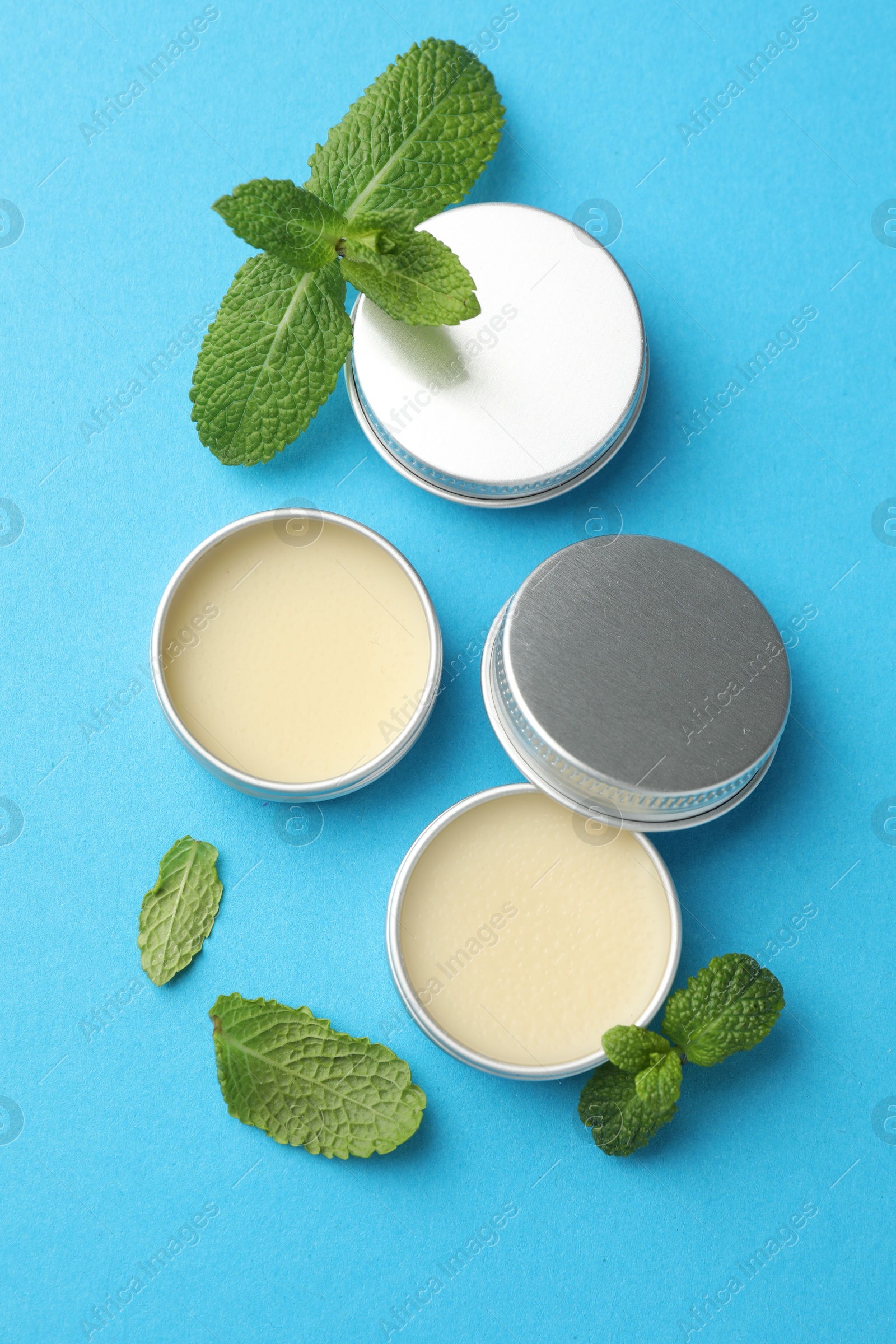 Photo of Natural lip balms and mint leaves on light blue background, flat lay