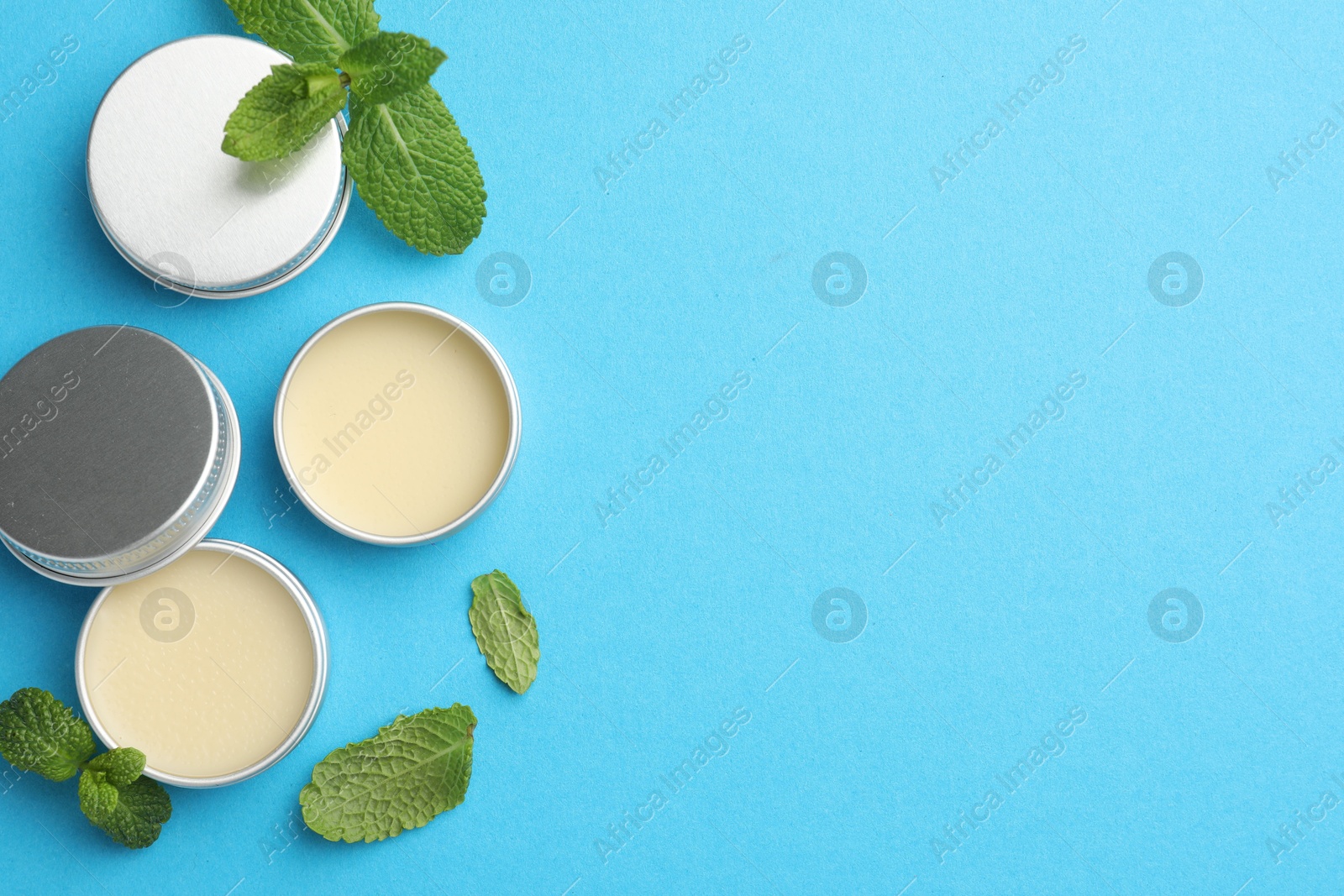 Photo of Natural lip balms and mint leaves on light blue background, flat lay. Space for text