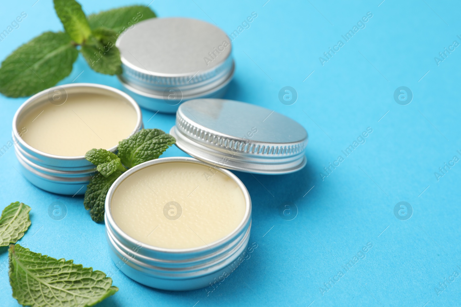 Photo of Natural lip balms and mint leaves on light blue background, closeup