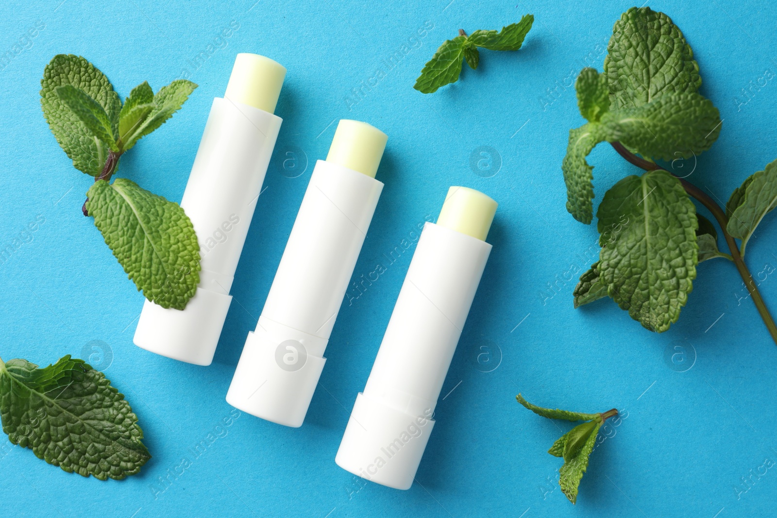 Photo of Natural lip balms and mint leaves on light blue background, flat lay