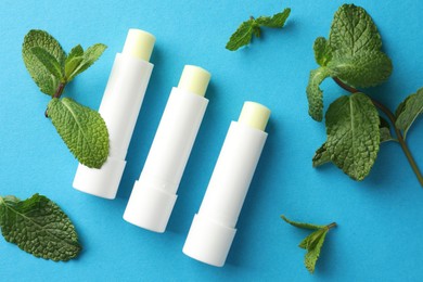 Photo of Natural lip balms and mint leaves on light blue background, flat lay