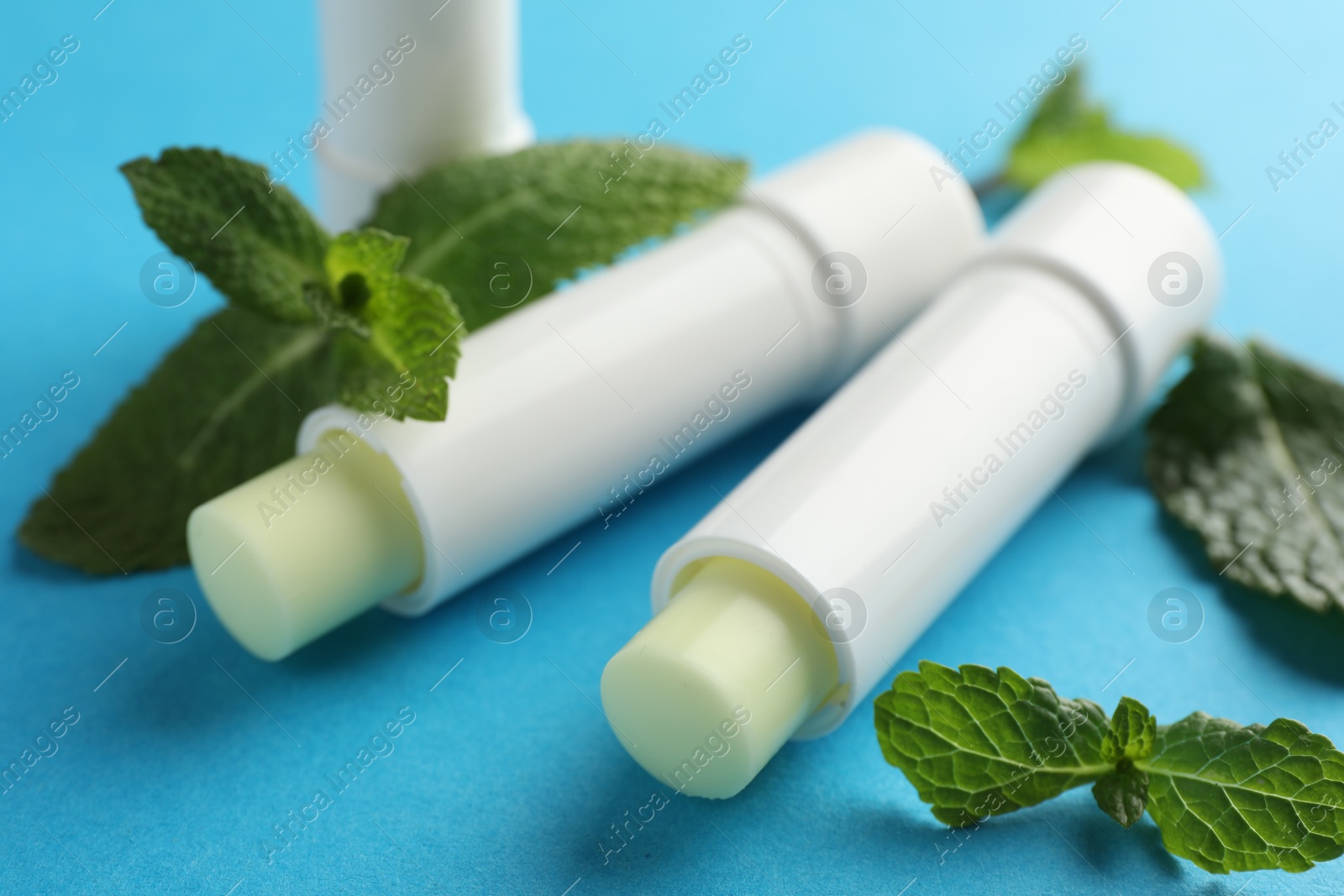 Photo of Natural lip balms and mint leaves on light blue background, closeup