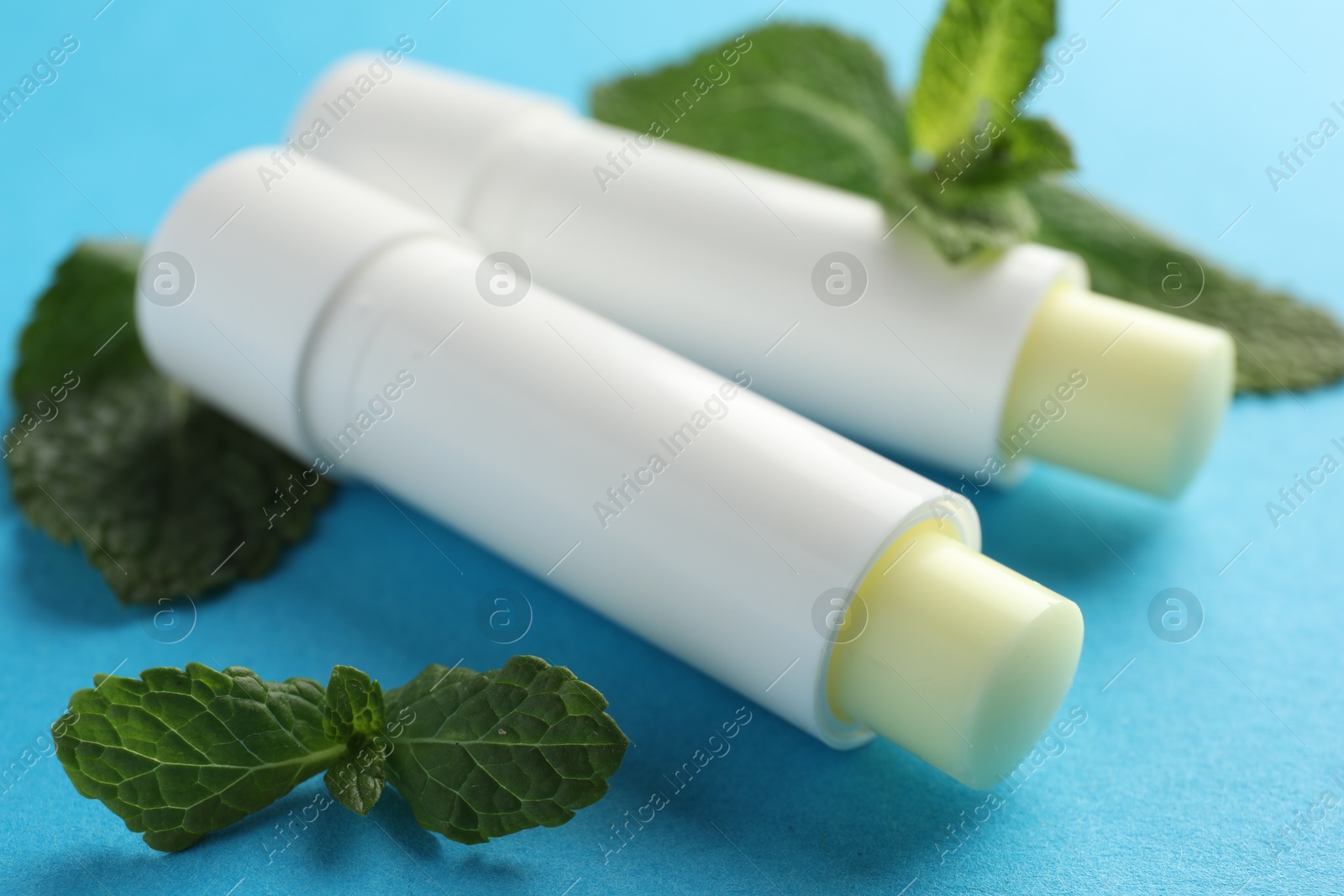 Photo of Natural lip balms and mint leaves on light blue background, closeup