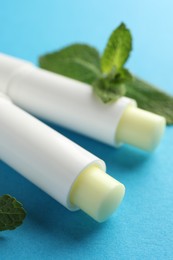 Photo of Natural lip balms and mint leaves on light blue background, closeup