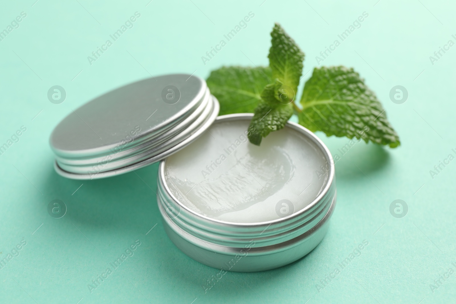 Photo of Natural lip balm and mint leaves on turquoise background, closeup