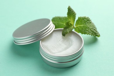 Photo of Natural lip balm and mint leaves on turquoise background, closeup