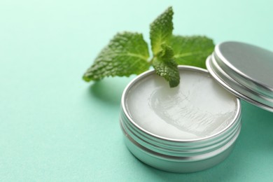 Photo of Natural lip balm and mint leaves on turquoise background, closeup. Space for text