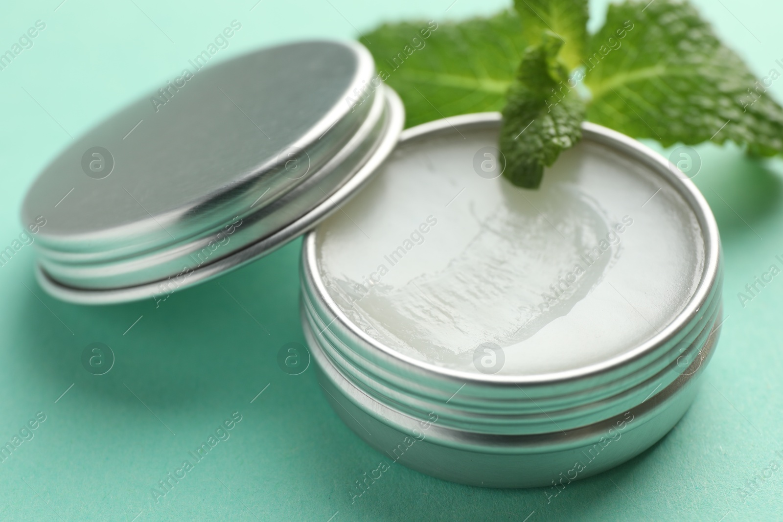 Photo of Natural lip balm and mint leaves on turquoise background, closeup