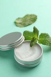 Photo of Natural lip balm and mint leaves on turquoise background, closeup