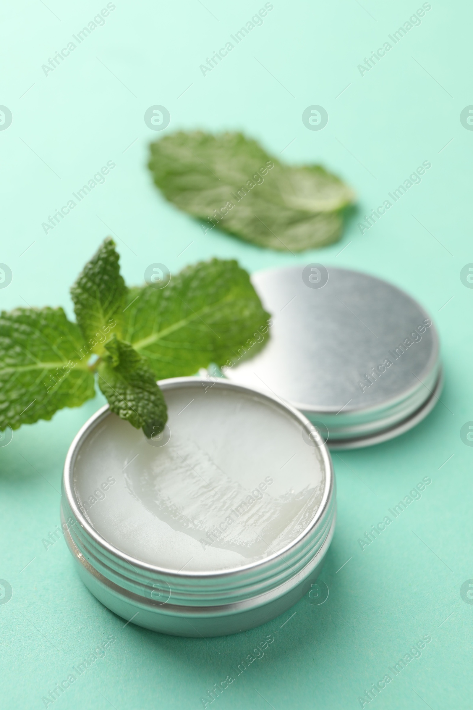 Photo of Natural lip balm and mint leaves on turquoise background, closeup