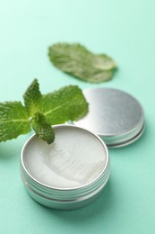 Photo of Natural lip balm and mint leaves on turquoise background, closeup