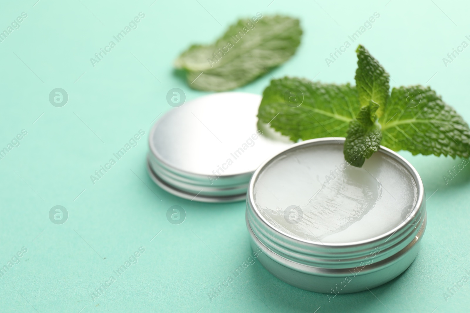 Photo of Natural lip balm and mint leaves on turquoise background, closeup. Space for text