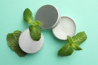 Photo of Natural lip balms and mint leaves on turquoise background, flat lay