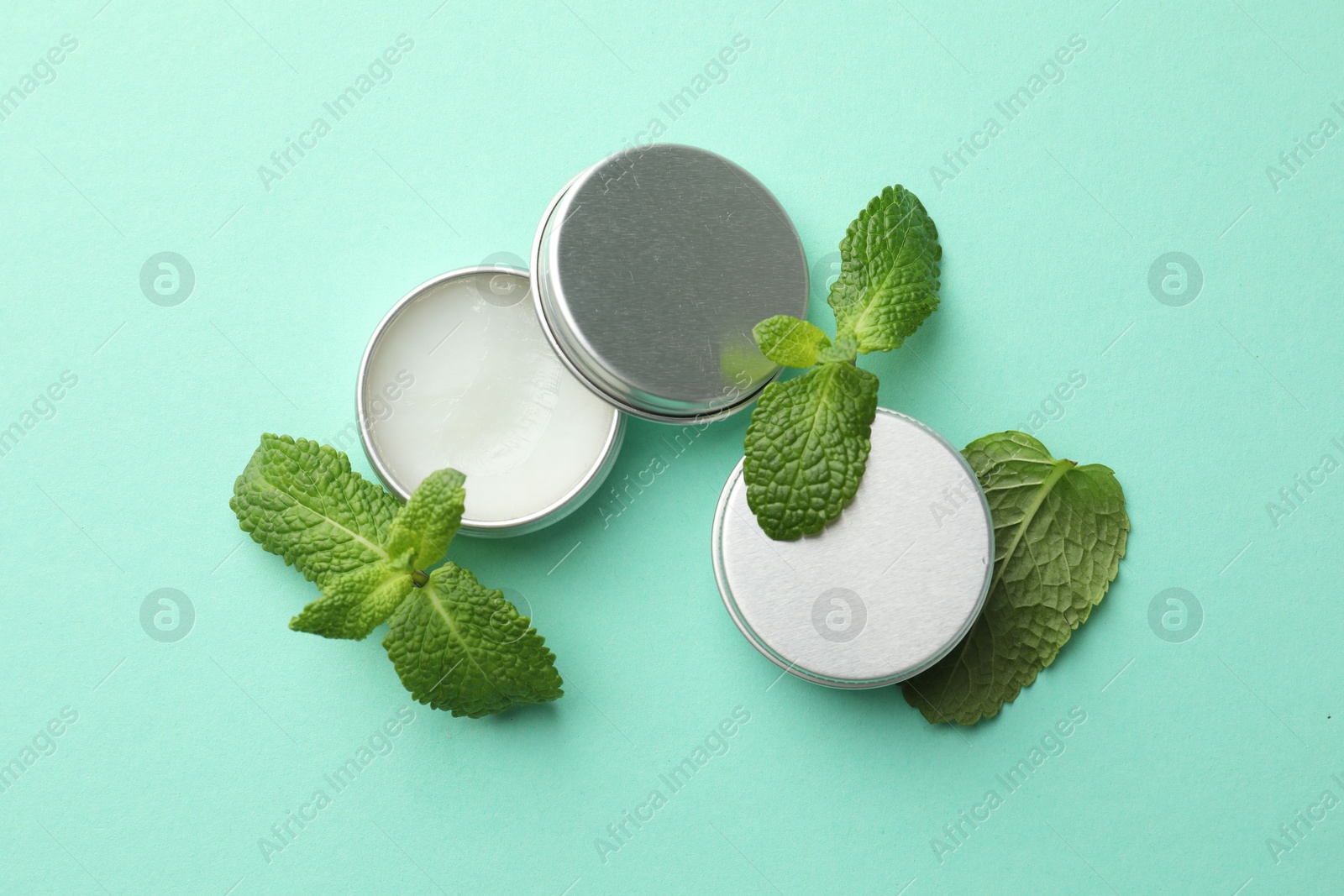 Photo of Natural lip balms and mint leaves on turquoise background, flat lay