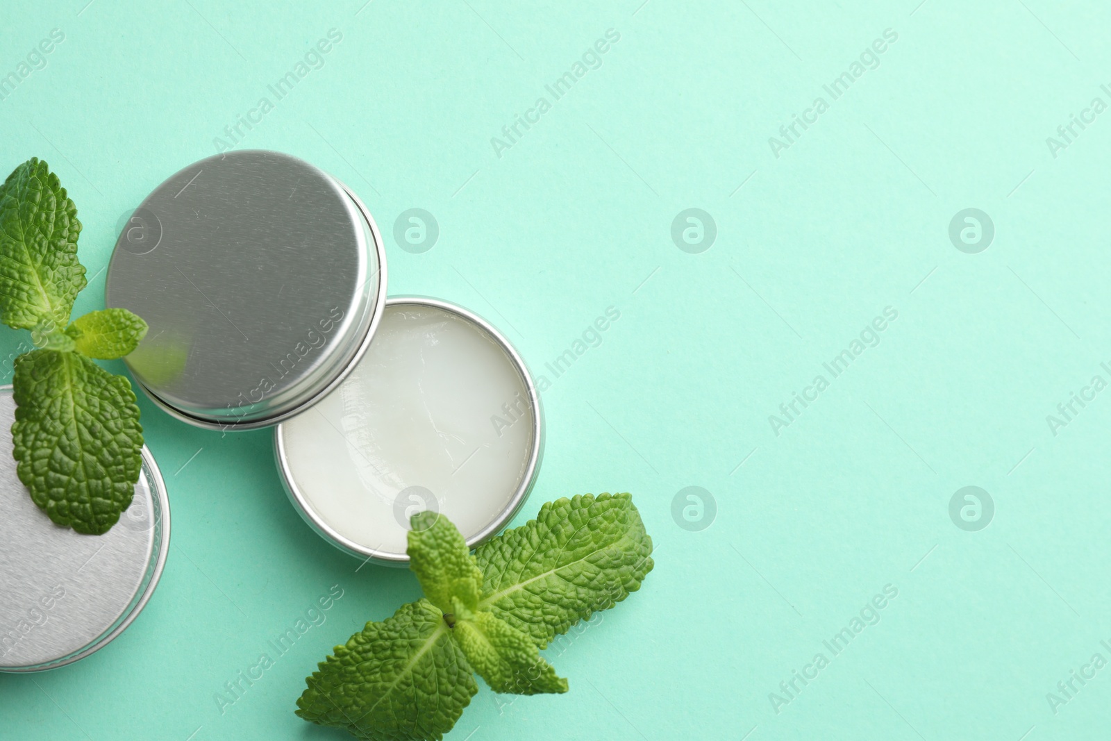 Photo of Natural lip balms and mint leaves on turquoise background, flat lay. Space for text