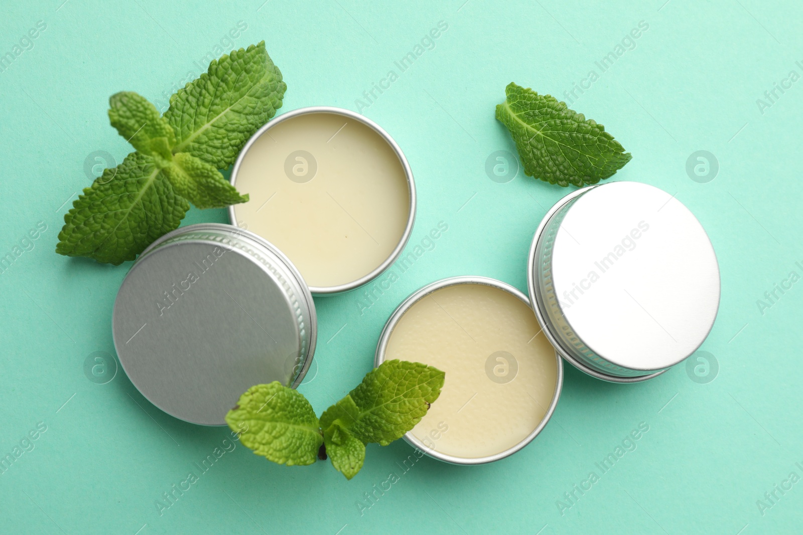 Photo of Natural lip balms and mint leaves on turquoise background, flat lay