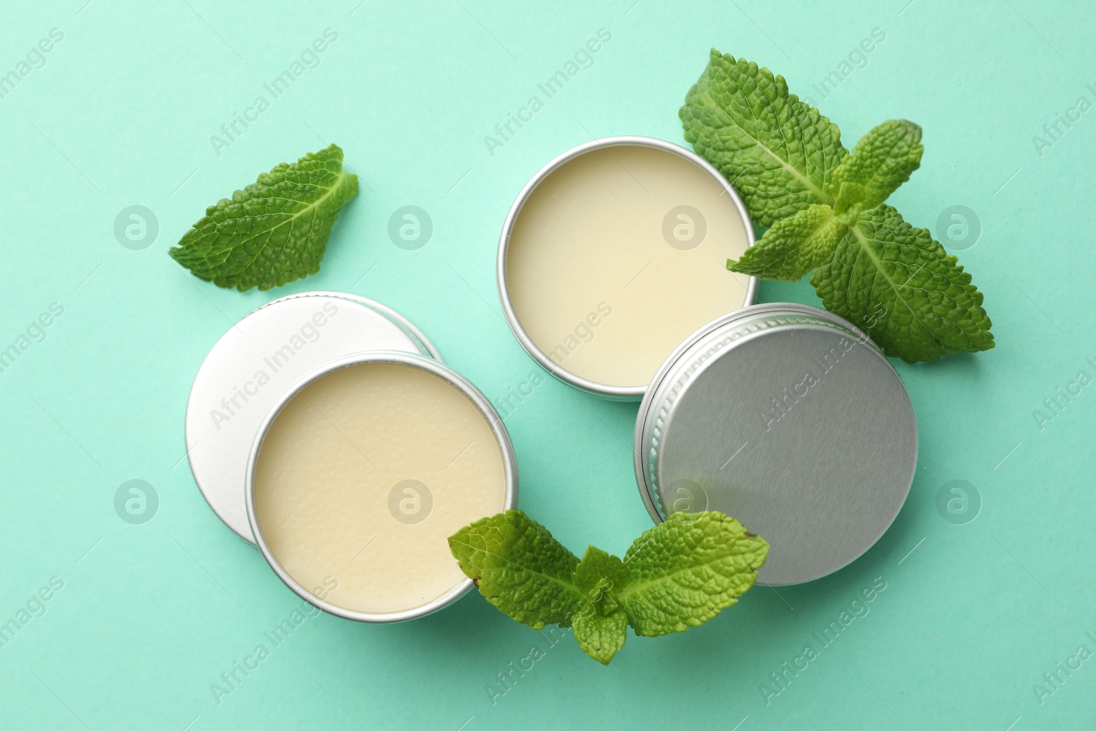 Photo of Natural lip balms and mint leaves on turquoise background, flat lay