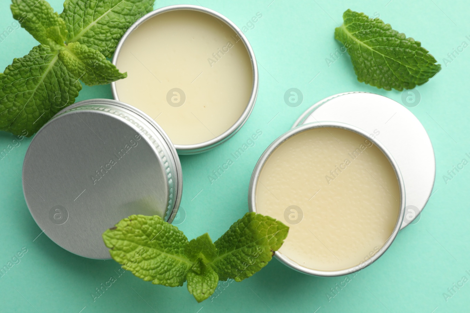 Photo of Natural lip balms and mint leaves on turquoise background, flat lay