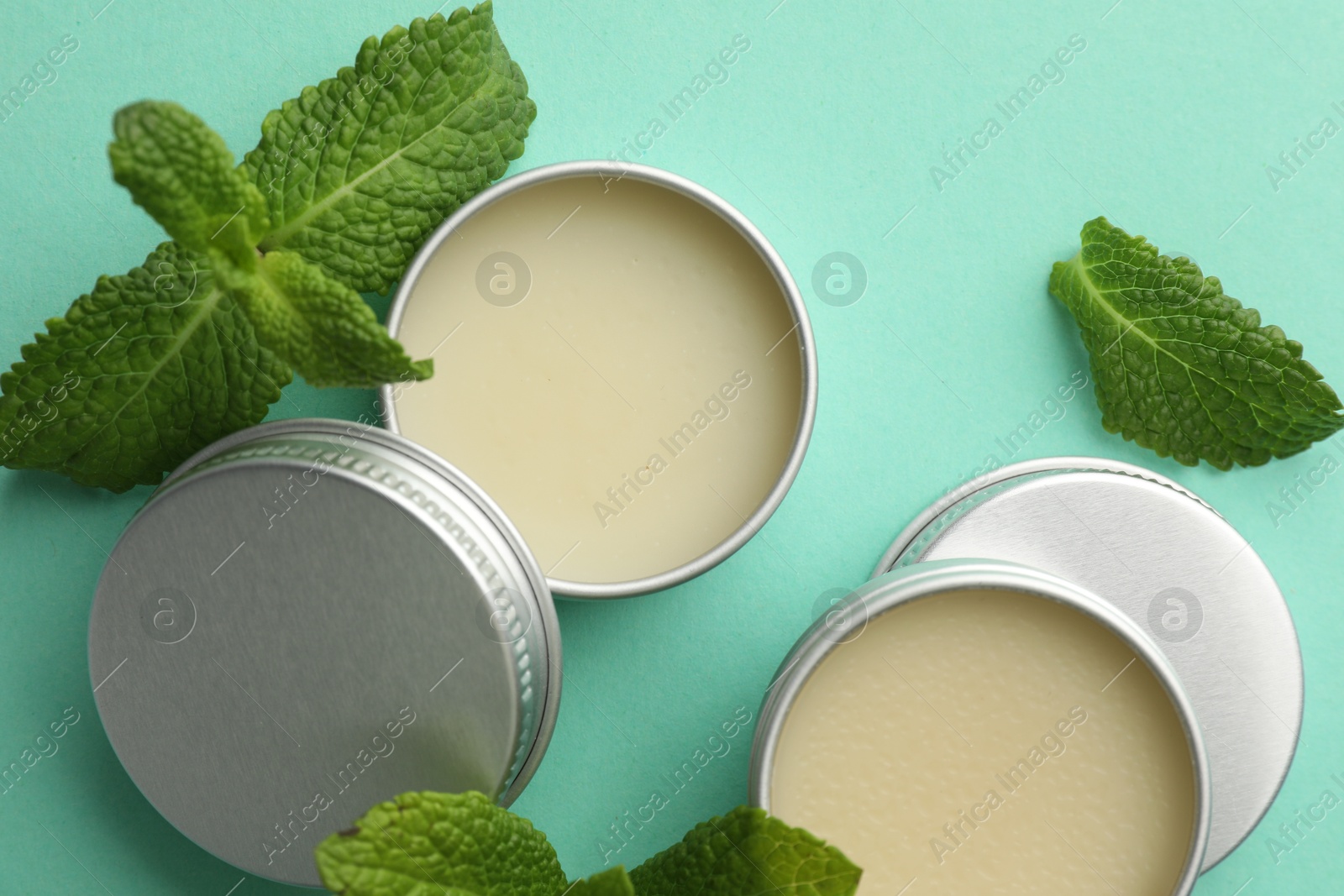 Photo of Natural lip balms and mint leaves on turquoise background, flat lay