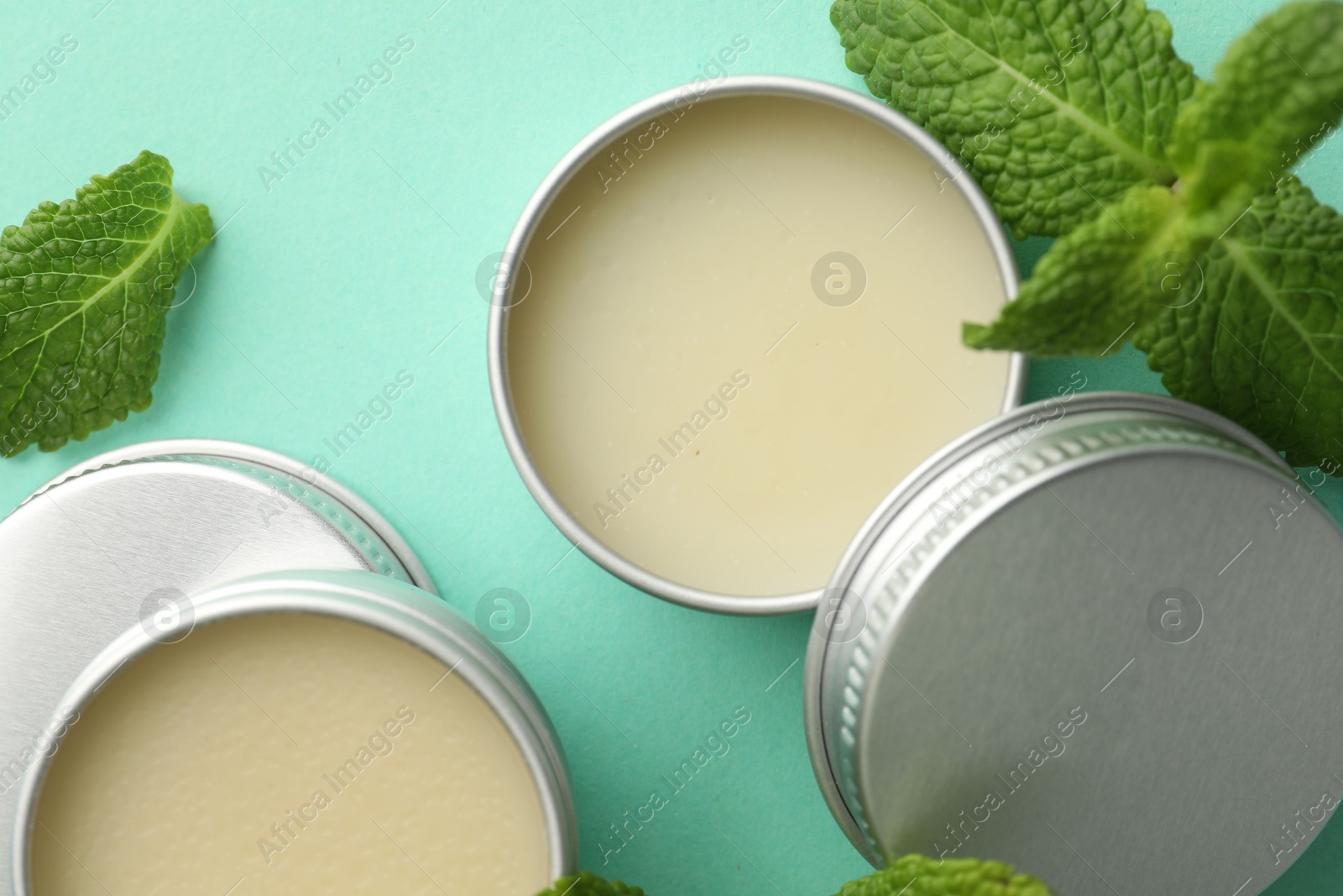 Photo of Natural lip balms and mint leaves on turquoise background, flat lay