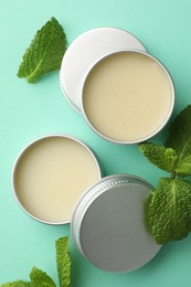 Photo of Natural lip balms and mint leaves on turquoise background, flat lay