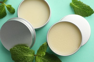 Photo of Natural lip balms and mint leaves on turquoise background, flat lay