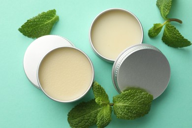 Photo of Natural lip balms and mint leaves on turquoise background, flat lay