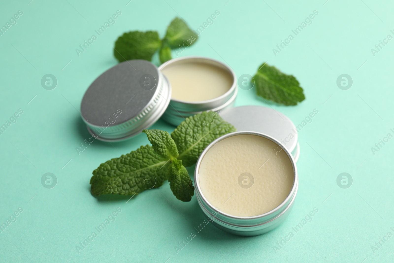 Photo of Natural lip balms and mint leaves on turquoise background