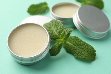 Photo of Natural lip balms and mint leaves on turquoise background, closeup