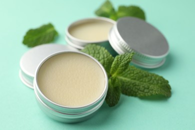 Photo of Natural lip balms and mint leaves on turquoise background, closeup