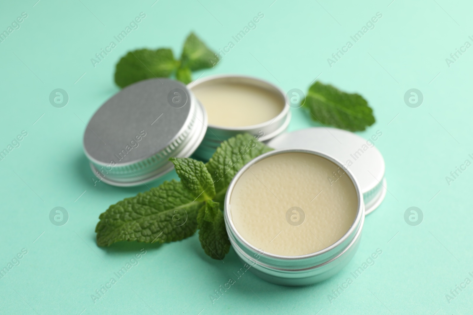 Photo of Natural lip balms and mint leaves on turquoise background, closeup