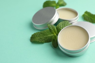 Photo of Natural lip balms and mint leaves on turquoise background, closeup. Space for text