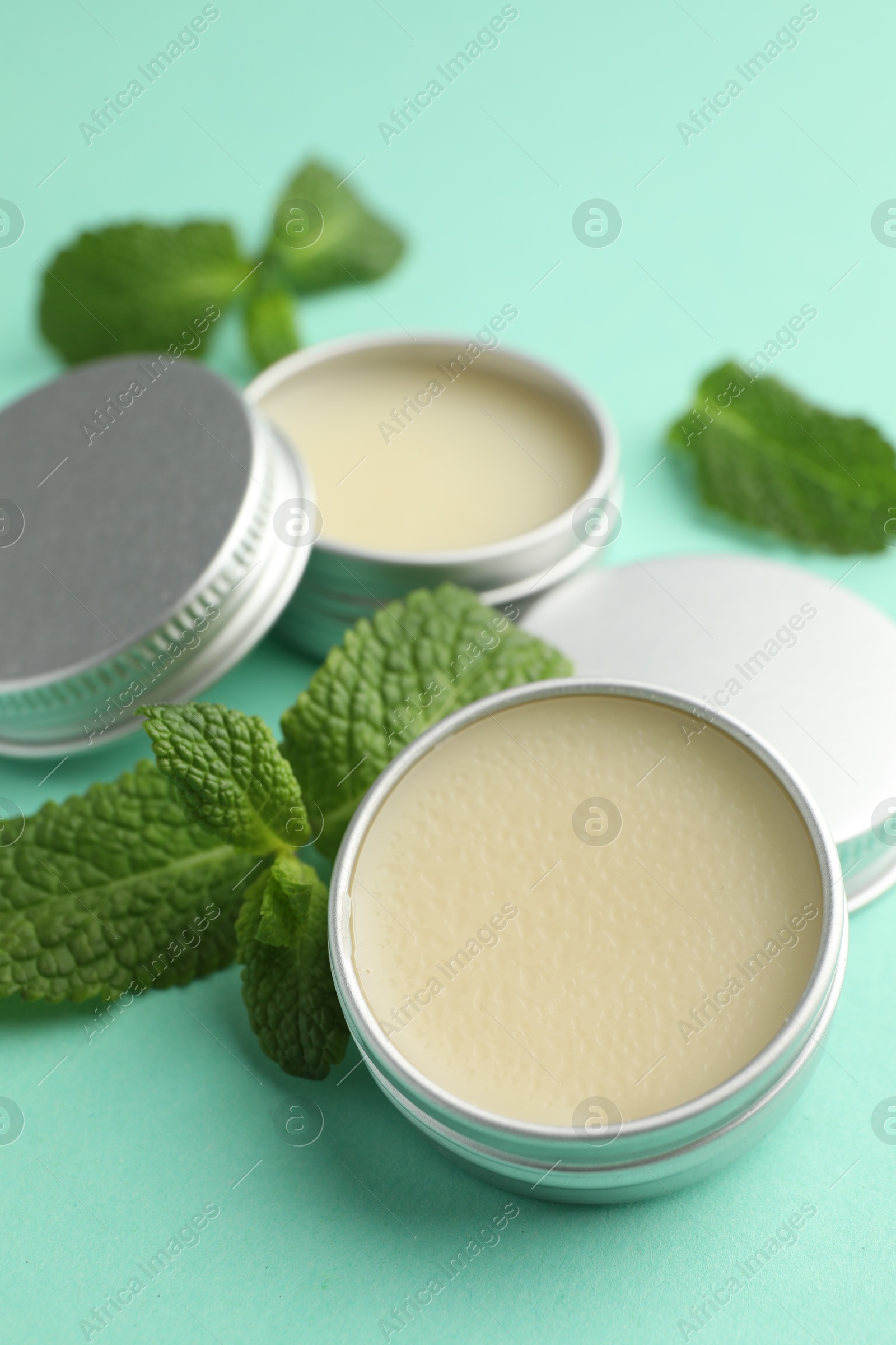 Photo of Natural lip balms and mint leaves on turquoise background, closeup