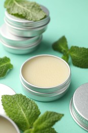 Photo of Natural lip balms and mint leaves on turquoise background, closeup