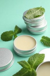 Photo of Natural lip balms and mint leaves on turquoise background, closeup