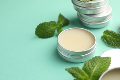 Photo of Natural lip balms and mint leaves on turquoise background, closeup. Space for text