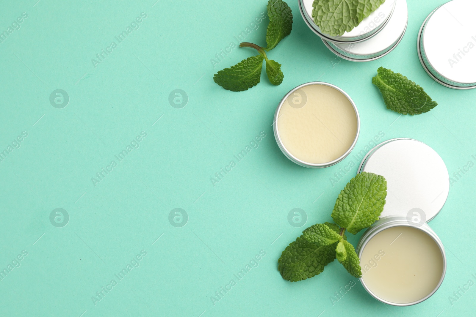 Photo of Natural lip balms and mint leaves on turquoise background, flat lay. Space for text