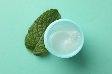 Photo of Natural lip balm and mint leaf on turquoise background, top view