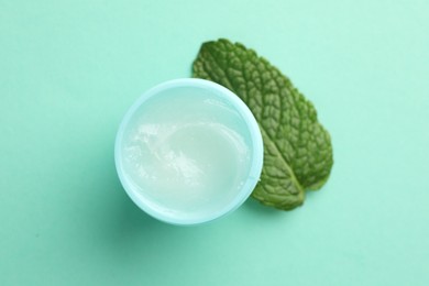 Photo of Natural lip balm and mint leaf on turquoise background, top view