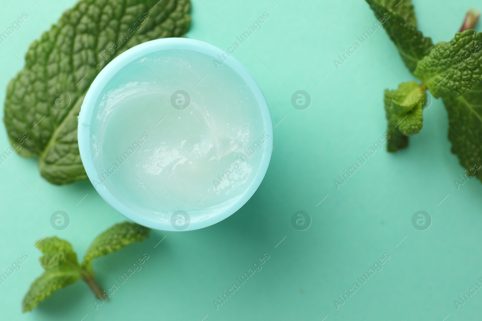 Photo of Natural lip balm and mint leaves on turquoise background, top view