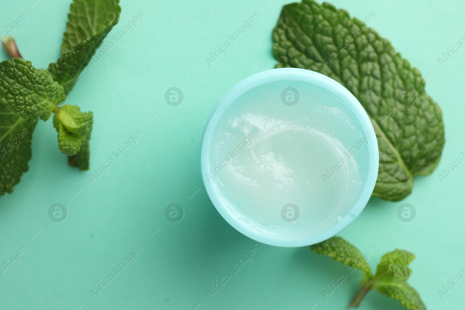 Photo of Natural lip balm and mint leaves on turquoise background, top view