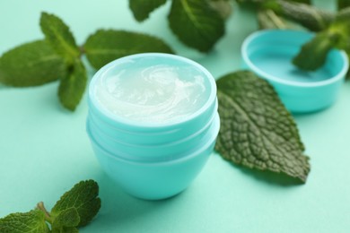 Photo of Natural lip balm and mint leaves on turquoise background, closeup