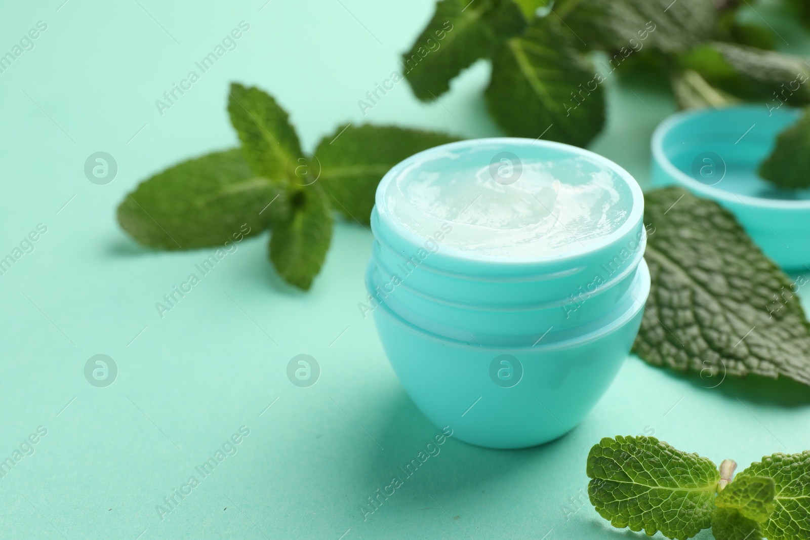 Photo of Natural lip balm and mint leaves on turquoise background, closeup. Space for text