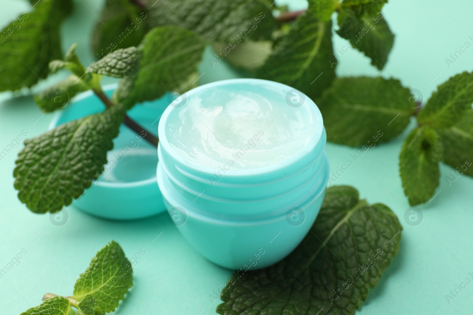 Photo of Natural lip balm and mint leaves on turquoise background, closeup