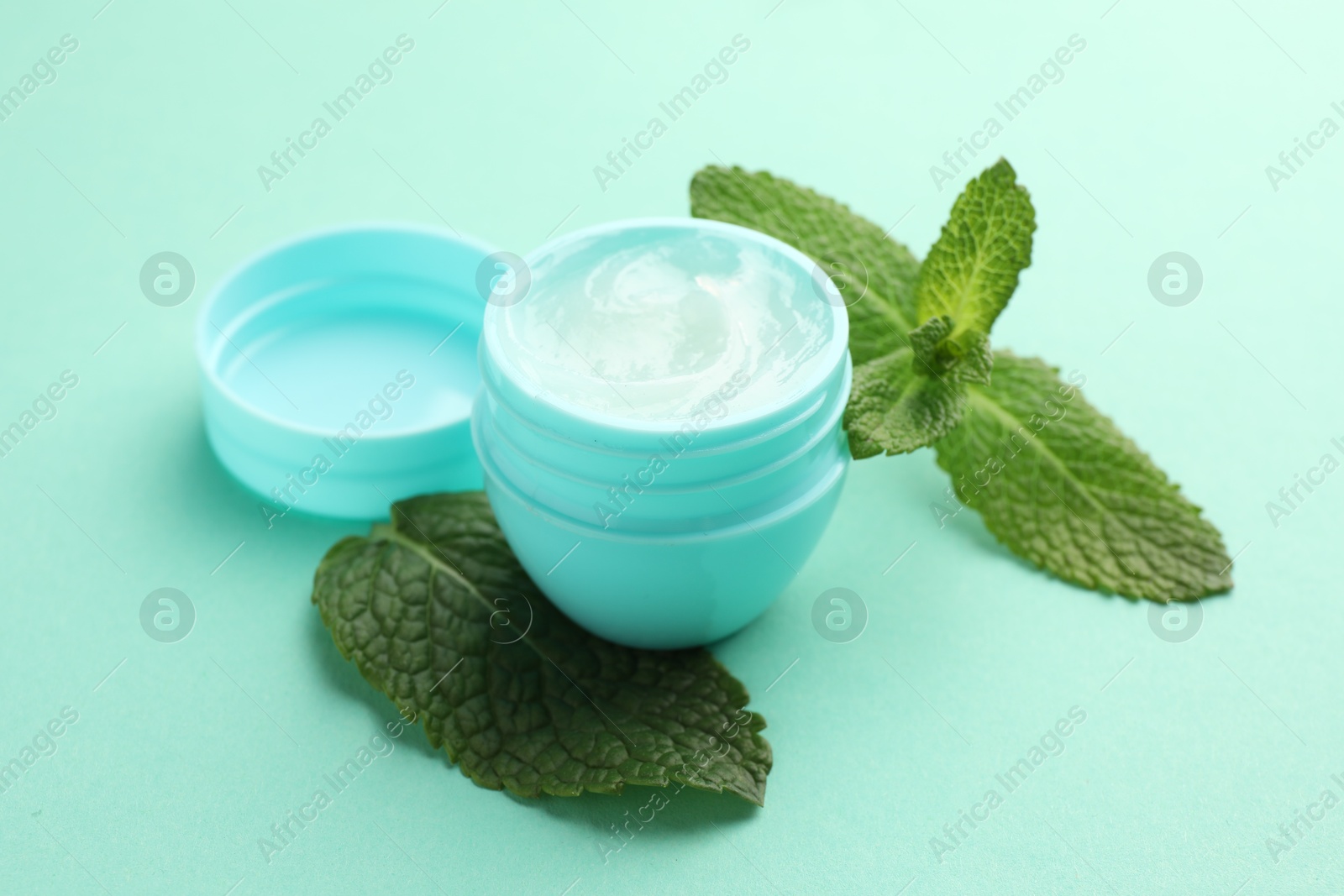 Photo of Natural lip balm and mint leaves on turquoise background, closeup