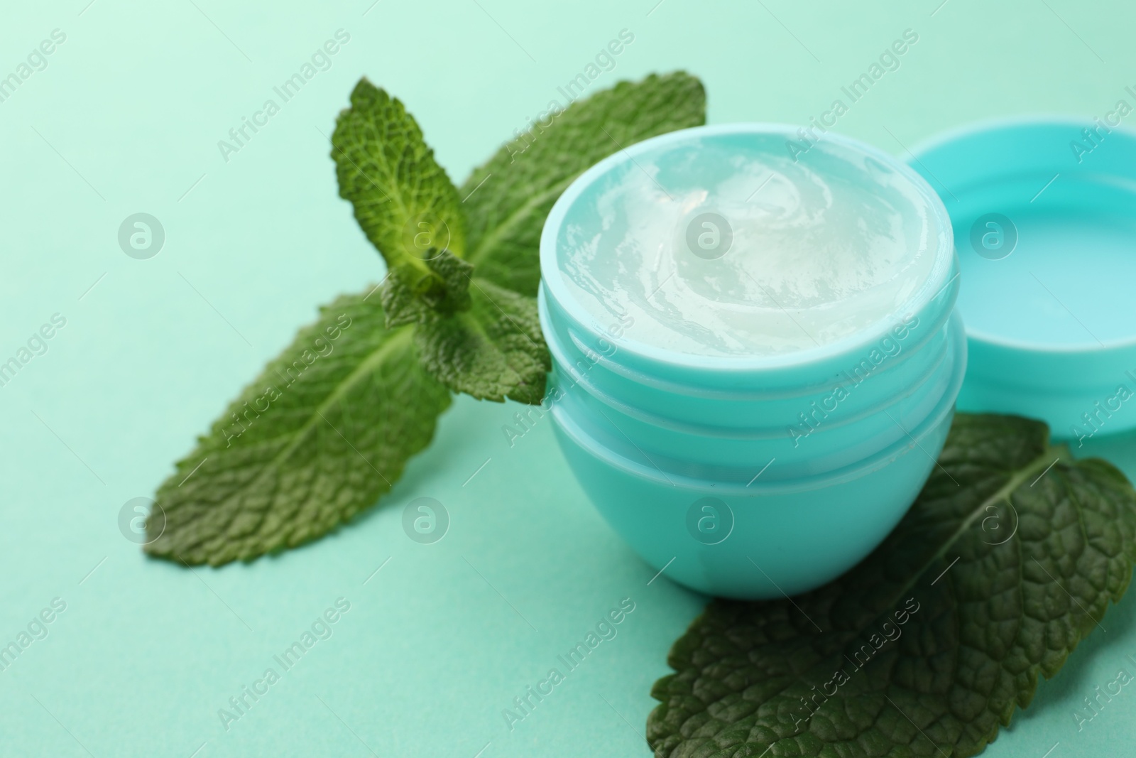 Photo of Natural lip balm and mint leaves on turquoise background, closeup