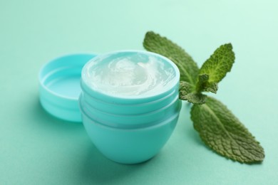 Photo of Natural lip balm and mint leaves on turquoise background, closeup